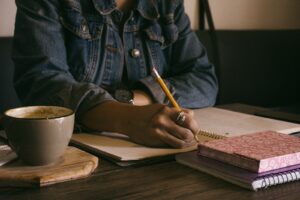 Person sat drinking coffee and writing in a notebook